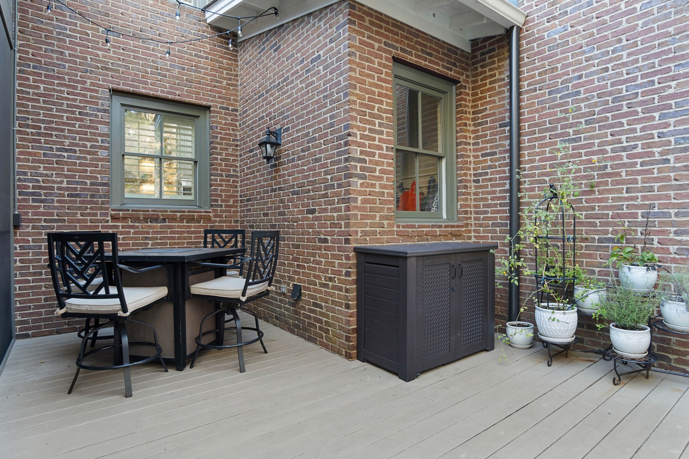 Private brick courtyard with a small dining set, potted plants, and a light wood deck