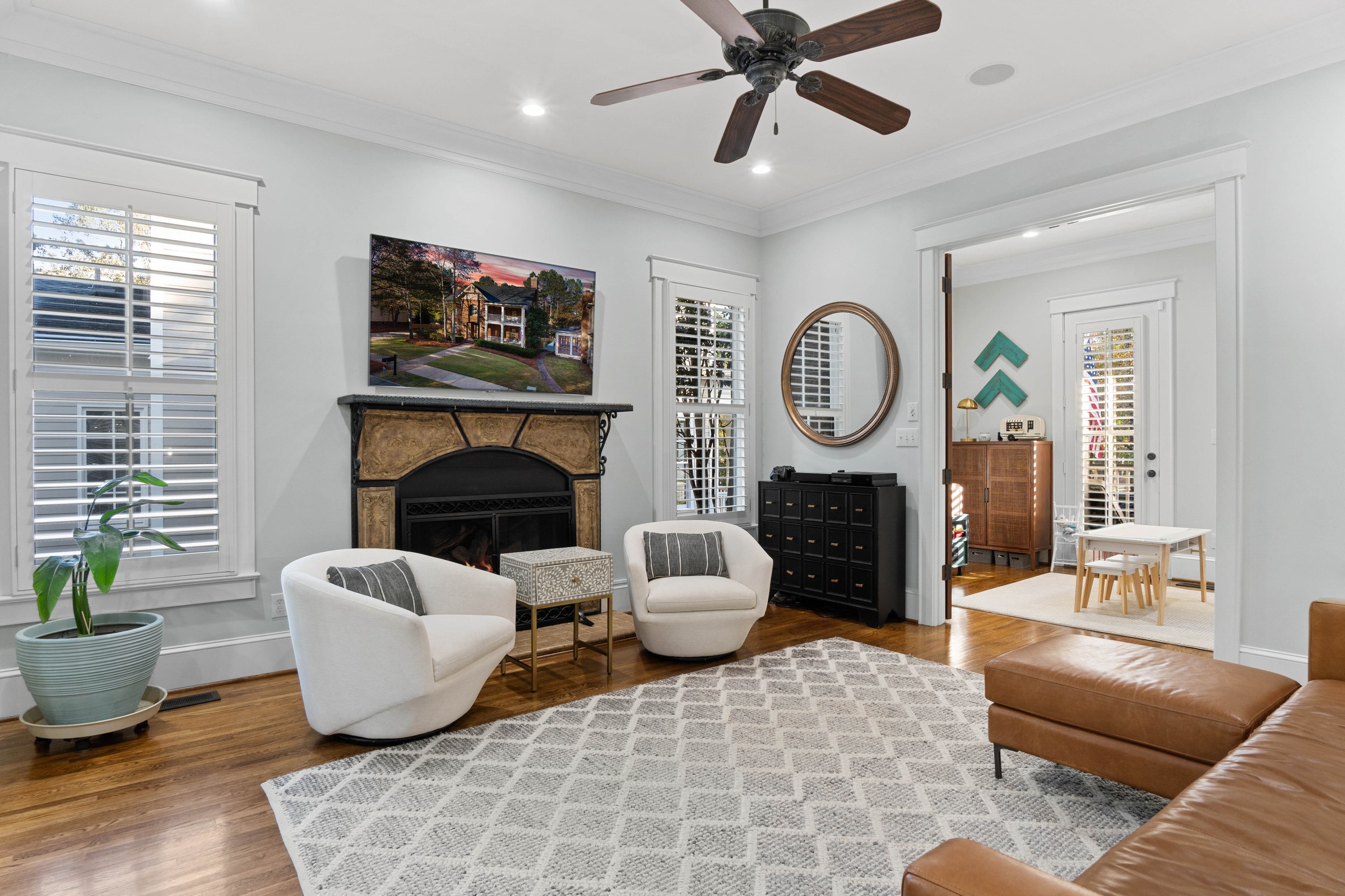 Bright sitting room arranged around a fireplace with white lounge chairs and warm wood floors