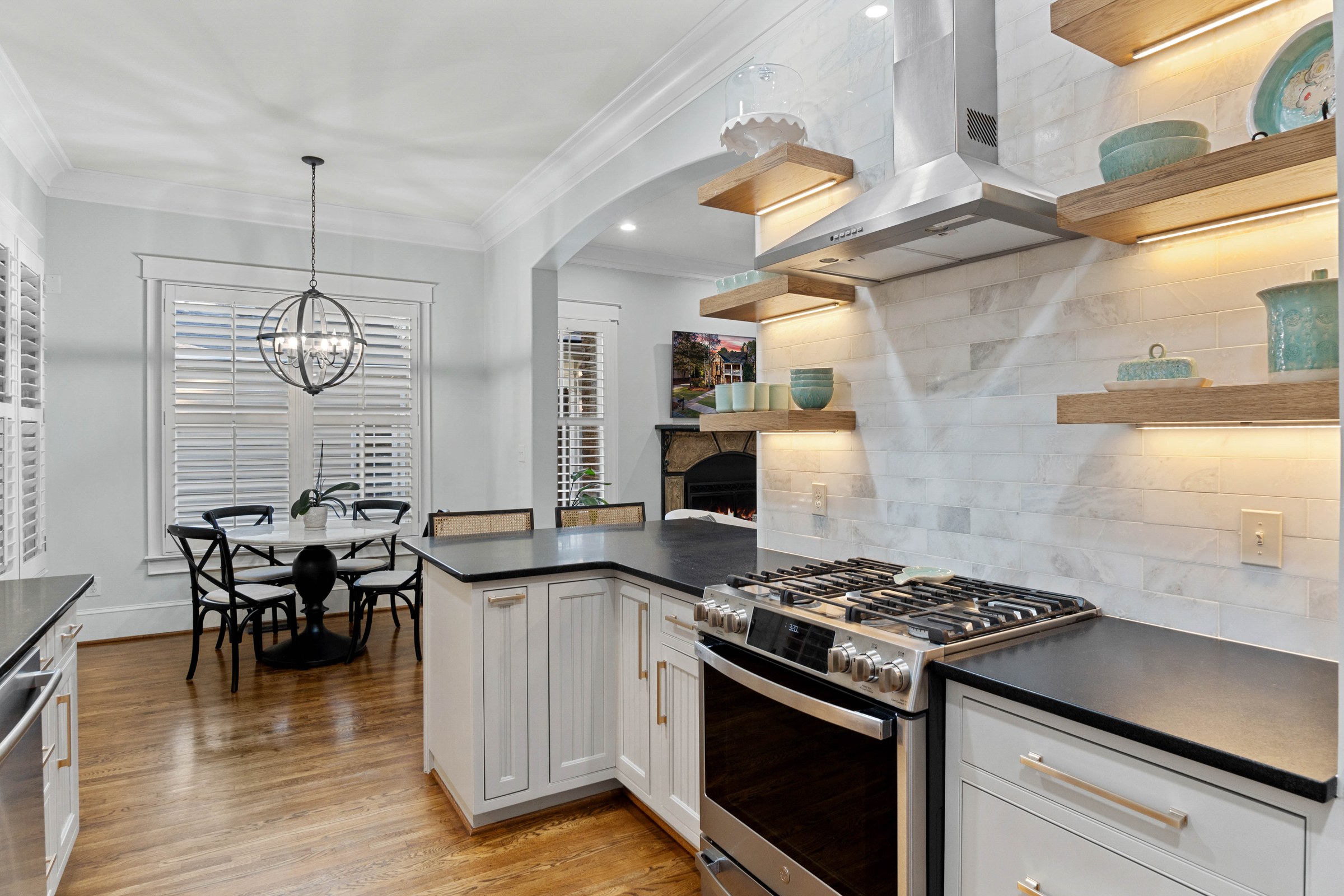 White kitchen with a black island, brass-lit open shelves, and an adjoining breakfast area