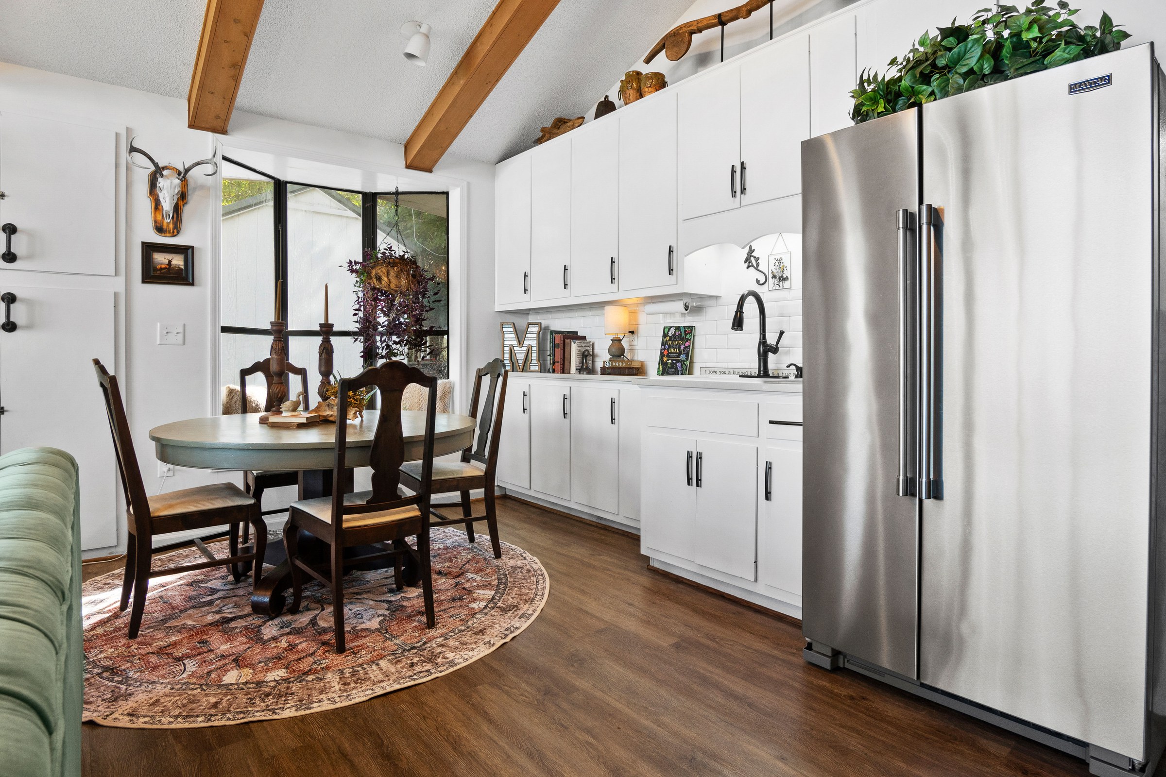 White lakeside kitchen with exposed ceiling beams, a stainless refrigerator, and dining table
