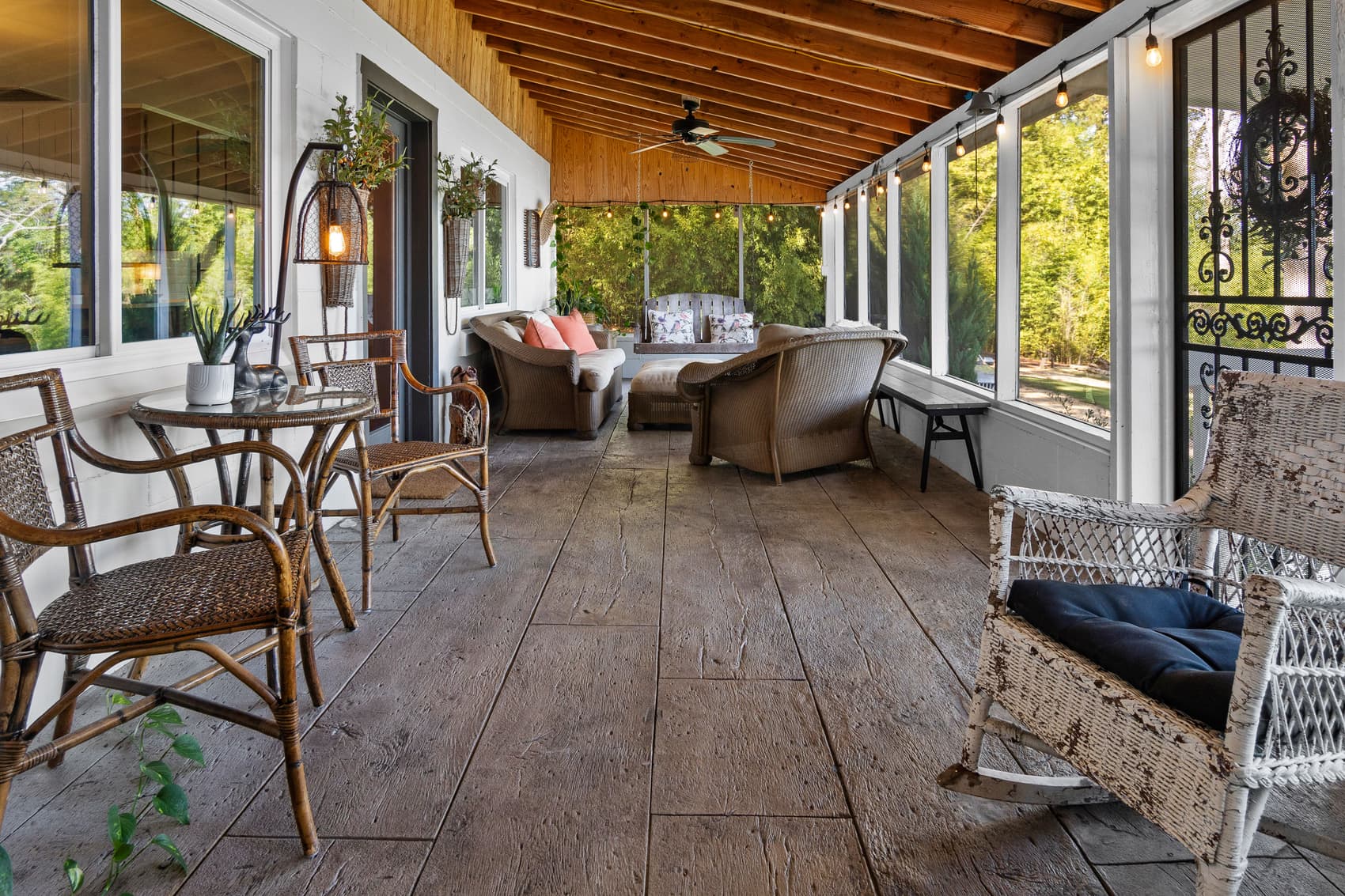 Long screened porch with string lights, wicker seating, and a swing overlooking the yard