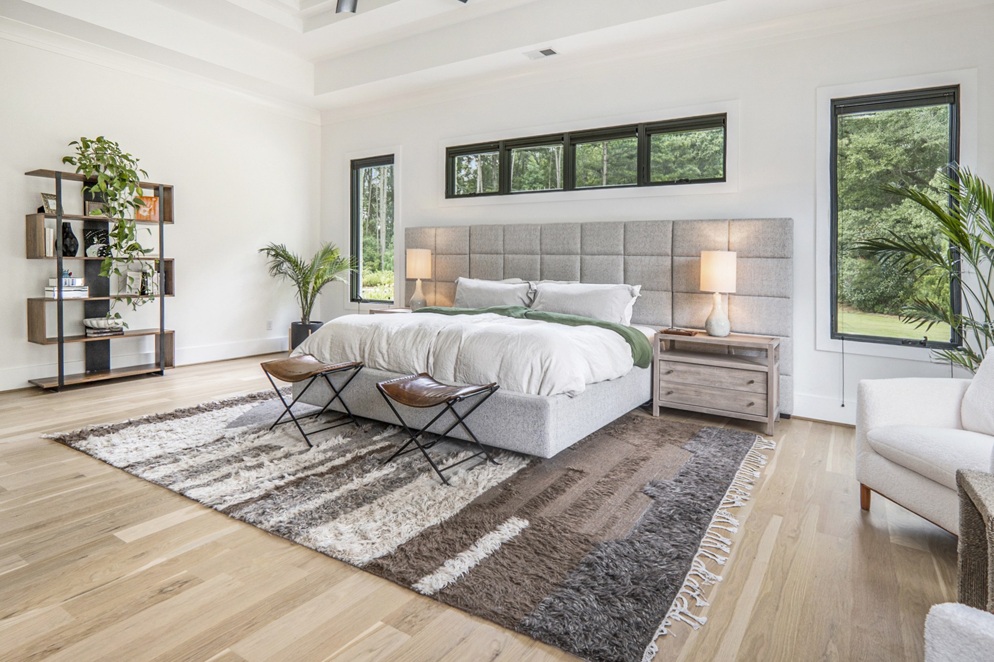 Bright primary bedroom with a gray upholstered bed, black-framed windows, and pale wood floors